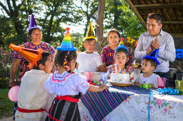 Wall Mural - Latin girl blows out the candles at her birthday celebration, her friends and family accompany her with joy.