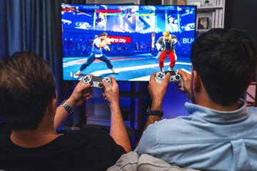 Wall Mural - Friend gamers playing video game of battle martial arts fighter on TV using joysticks position of backside background. Comfy living neon light at home place with cheerful fighting winner. Sellable.