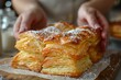Close-up of hands holding flaky pastry near mouth with powdered sugar