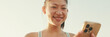 © Andrii Nekrasov - Close-up of smiling asian girl in sports top using cellphone while standing on waterfront on modern buildings background in morning light, Panorama