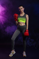 Canvas Print - Beautiful woman wearing boxing gloves in color lights and smoke on black background