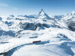 A stunning aerial shot of Zermatt ski resort, featuring a red train crossing snowy terrain with the Matterhorn peak and a clear blue sky in the backdrop. It showcases the Swiss Alps' winter beauty.