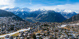 Fototapeta  - Aerial panoramic view of Verbier, Switzerland, showcasing a mix of snow covered and green landscapes in a valley. Traditional alpine architecture fills the town, indicating a seasonal transition.