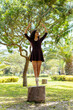 Young woman in ballet attire strikes a dance pose on a tree stump, surrounded by nature