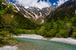 Snow covered mountain peaks with a green forest and fast flowing river below