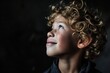 Portrait of a cute little boy with curly hair on a dark background