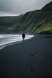 A person walking alone on black sand beach