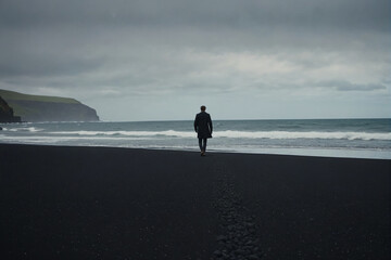Wall Mural - A person walking alone on black sand beach