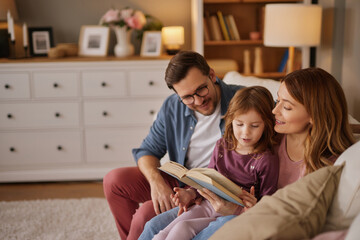 Family with little daughter reading book on sofa in living room