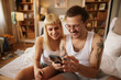 Tattooed man and his girlfriend using mobile phone in bedroom