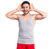 Young handsome man wearing swimwear and sleeveless t-shirt smiling cheerful playing peek a boo with hands showing face. surprised and exited
