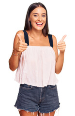 Wall Mural - Young hispanic woman wearing casual clothes success sign doing positive gesture with hand, thumbs up smiling and happy. cheerful expression and winner gesture.