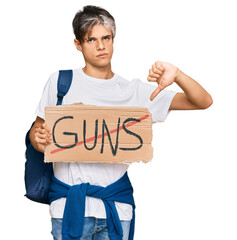 Wall Mural - Young hispanic man holding no guns warning banner with angry face, negative sign showing dislike with thumbs down, rejection concept