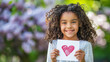 Adorable Girl Surrounded by Common Lilac Flowers Holding a Mother's Day Card with Hand Drawn Red Heart. Lovely Background with Copy Space.
