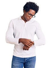 Sticker - Handsome african american man with afro hair wearing casual clothes and glasses checking the time on wrist watch, relaxed and confident