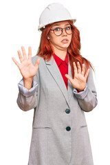 Canvas Print - Young redhead woman wearing architect hardhat afraid and terrified with fear expression stop gesture with hands, shouting in shock. panic concept.