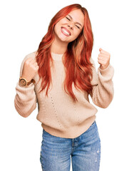 Wall Mural - Young redhead woman wearing casual winter sweater very happy and excited doing winner gesture with arms raised, smiling and screaming for success. celebration concept.