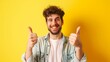 A portrait of a man holding his thumbs up against a yellow backdrop with a funny expression