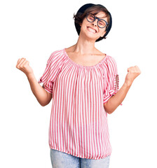 Wall Mural - Beautiful young woman with short hair wearing casual clothes and glasses very happy and excited doing winner gesture with arms raised, smiling and screaming for success. celebration concept.