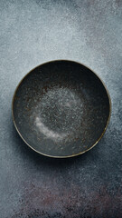 Ceramic dark round textured plate. Close up on gray concrete background. Free space for text.