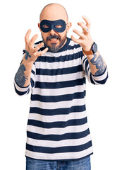 Wall Mural - Young handsome man wearing burglar mask shouting frustrated with rage, hands trying to strangle, yelling mad