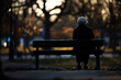 An elderly woman sits alone on a park bench, melancholy of social isolation and loneliness.