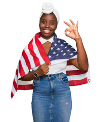 Wall Mural - Young african woman with turban holding united states flag doing ok sign with fingers, smiling friendly gesturing excellent symbol