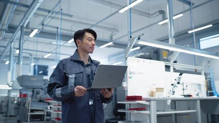 Leinwandbilder - Chief Engineer Walking Through the Hall in a Modern Factory with Manufacturing Machinery and Production Tools. Asian Specialist Holding a Laptop Computer. Successful Man in an Industrial Environment