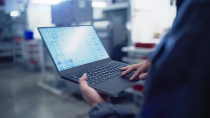 Aufkleber - Follow Footage with an Engineer Walking in a Factory and Using a Laptop Computer with Technical Drawing on Display. Specialist in Work Uniform Studying the Blueprint on Screen Before Manufacturing