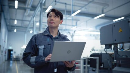 Leinwandbilder - Asian Engineer Using a Laptop Computer on the Go at Electronics Manufacturing Factory. Adult Technician Working on Daily Tasks and Analyzing New Production Plans. Cinematic Portrait