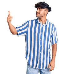 Sticker - Young hispanic man wearing casual clothes looking proud, smiling doing thumbs up gesture to the side