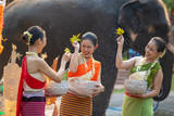 Fototapeta Sypialnia - Songkran festival. Northern Thai people in Traditional clothes dressing splashing water together in Songkran day cultural festival with elephant background.