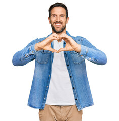 Canvas Print - Young handsome man wearing casual denim jacket smiling in love doing heart symbol shape with hands. romantic concept.