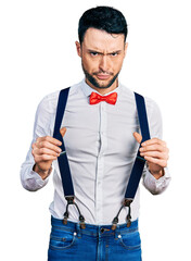 Canvas Print - Hispanic man with beard wearing hipster look holding suspenders skeptic and nervous, frowning upset because of problem. negative person.