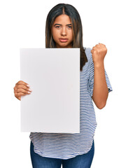 Poster - Young latin girl holding blank empty banner annoyed and frustrated shouting with anger, yelling crazy with anger and hand raised