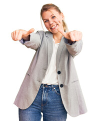 Wall Mural - Young beautiful blonde woman wearing elegant jacket approving doing positive gesture with hand, thumbs up smiling and happy for success. winner gesture.