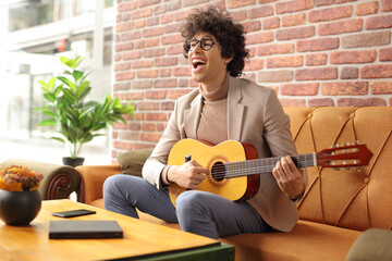 Sticker - Young man in a cafe sitting on a sofa and playing a guitar