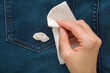 Young adult woman hand holding dry white paper napkin and removing chewing gum from dark blue jeans trousers. Closeup. Top down view.