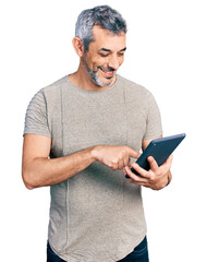 Middle age hispanic with grey hair using touchpad device smiling with a happy and cool smile on face. showing teeth.