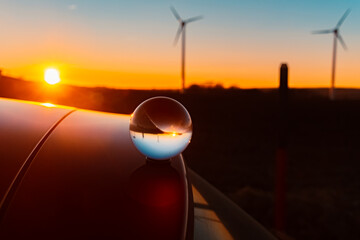 Wall Mural - Crystal ball sunset with wind power plant silhouettes and reflections on a car roof near Kugl, Dingolfing-Landau, Bavaria, Germany