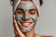 Smiling man applies a clay mask to the skin of his face isolated on gray background. Skin care concept, minimalistic studio photo.