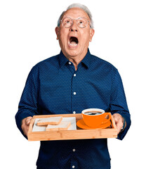 Canvas Print - Senior man with grey hair holding tray with lunch and coffee angry and mad screaming frustrated and furious, shouting with anger looking up.