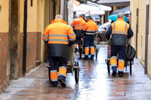 Men With Brooms And Cleaning Carts Walk The Streets, Removing Waste And Keeping The City Clean.