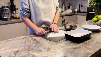 Wall Mural - A woman is preparing food on a countertop. She is cutting up some food on a cutting board. There are several bowls and a vase on the counter