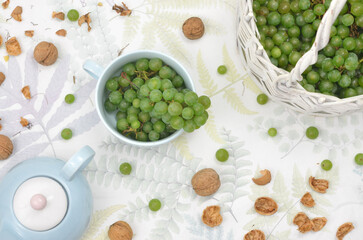 Wall Mural - Green grapes in a basket, nuts from a garden on a table with a blue kettle and cup. Top view.