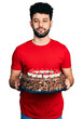 © Krakenimages.com - Young arab man with beard celebrating birthday holding big chocolate cake relaxed with serious expression on face. simple and natural looking at the camera.
