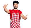 © Krakenimages.com - Young arab man with beard wearing cook apron looking at the camera smiling with open arms for hug. cheerful expression embracing happiness.