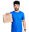 © Krakenimages.com - Young arab man with beard holding take away paper bag scared and amazed with open mouth for surprise, disbelief face
