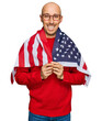 © Krakenimages.com - Bald man with beard wrapped around united states flag looking positive and happy standing and smiling with a confident smile showing teeth