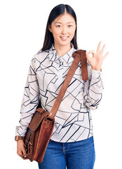 Poster - Young beautiful chinese woman holding briefcase doing ok sign with fingers, smiling friendly gesturing excellent symbol